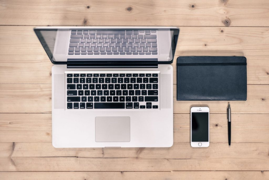 Tidy wooden desk with an open laptop, a notebook, a phone, and a pen