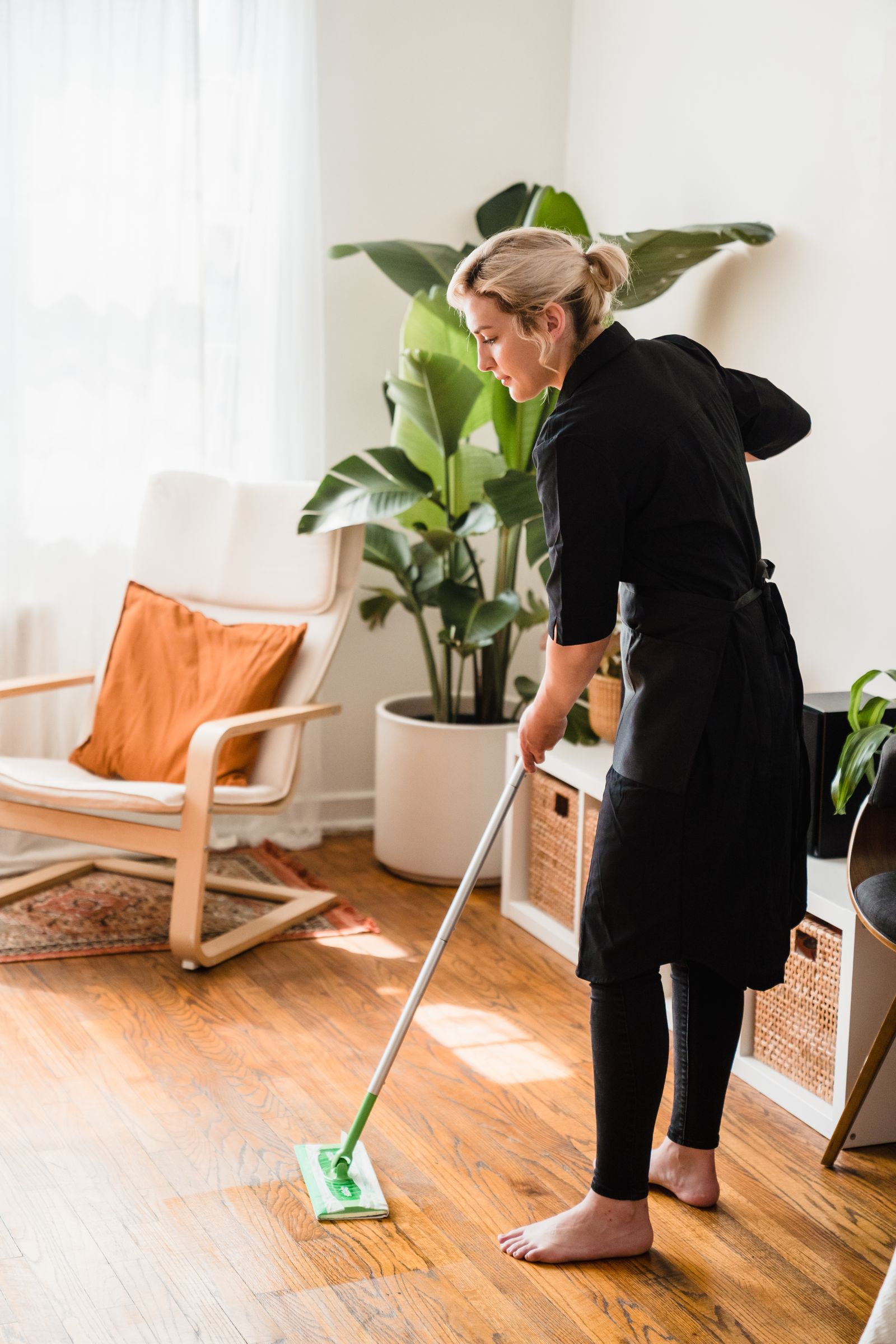 Woman mopping a wooden floor in a bright living room