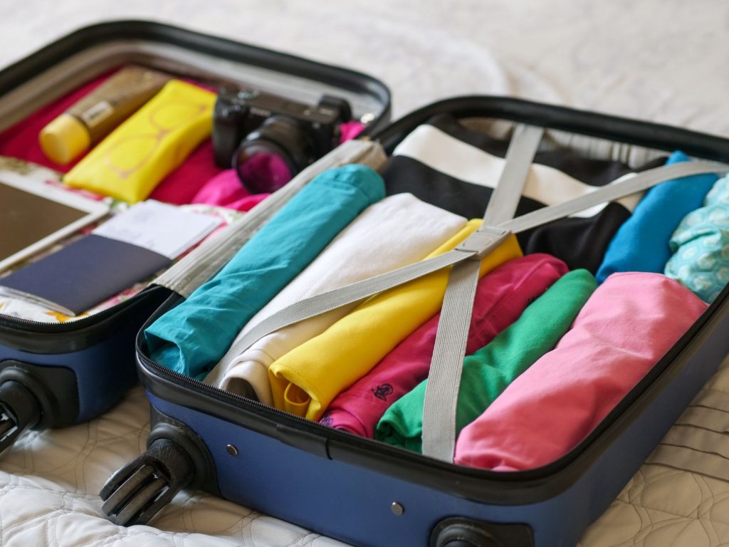 Open suitcase packed with rolled colorful clothes, a camera, and a passport