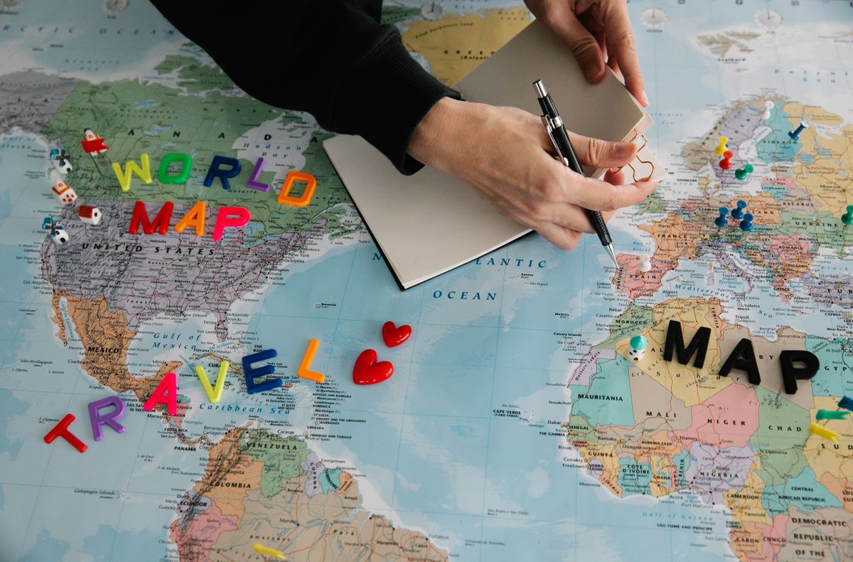 Hands planning a trip over a world map with a notebook