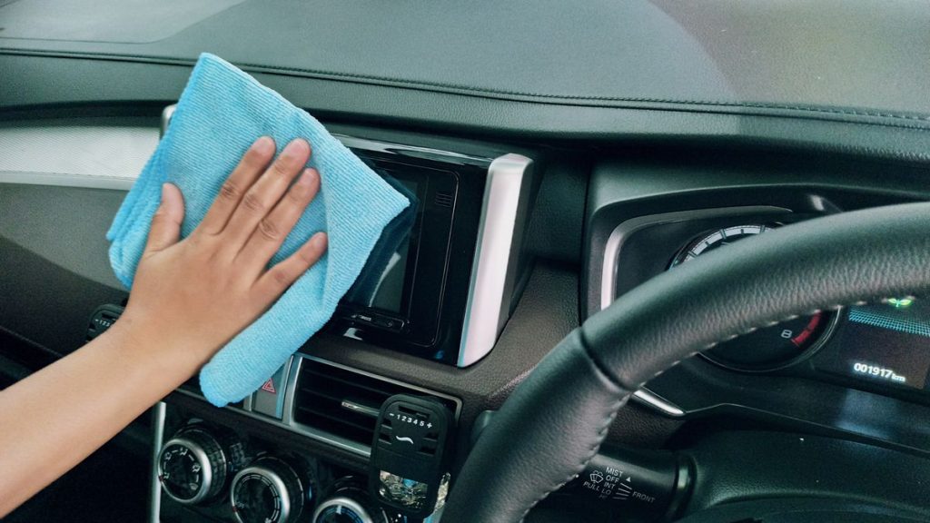 Hand wiping a car dashboard with a blue microfiber cloth