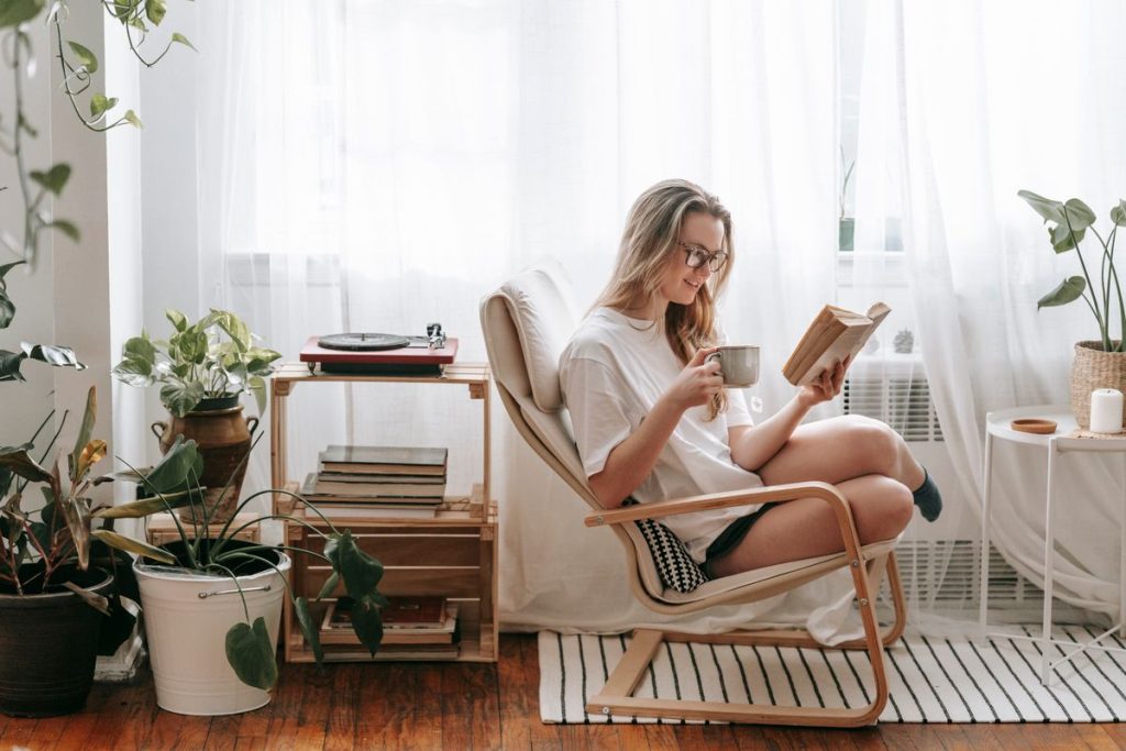 Woman reading a book in a cozy chair beside plants and books