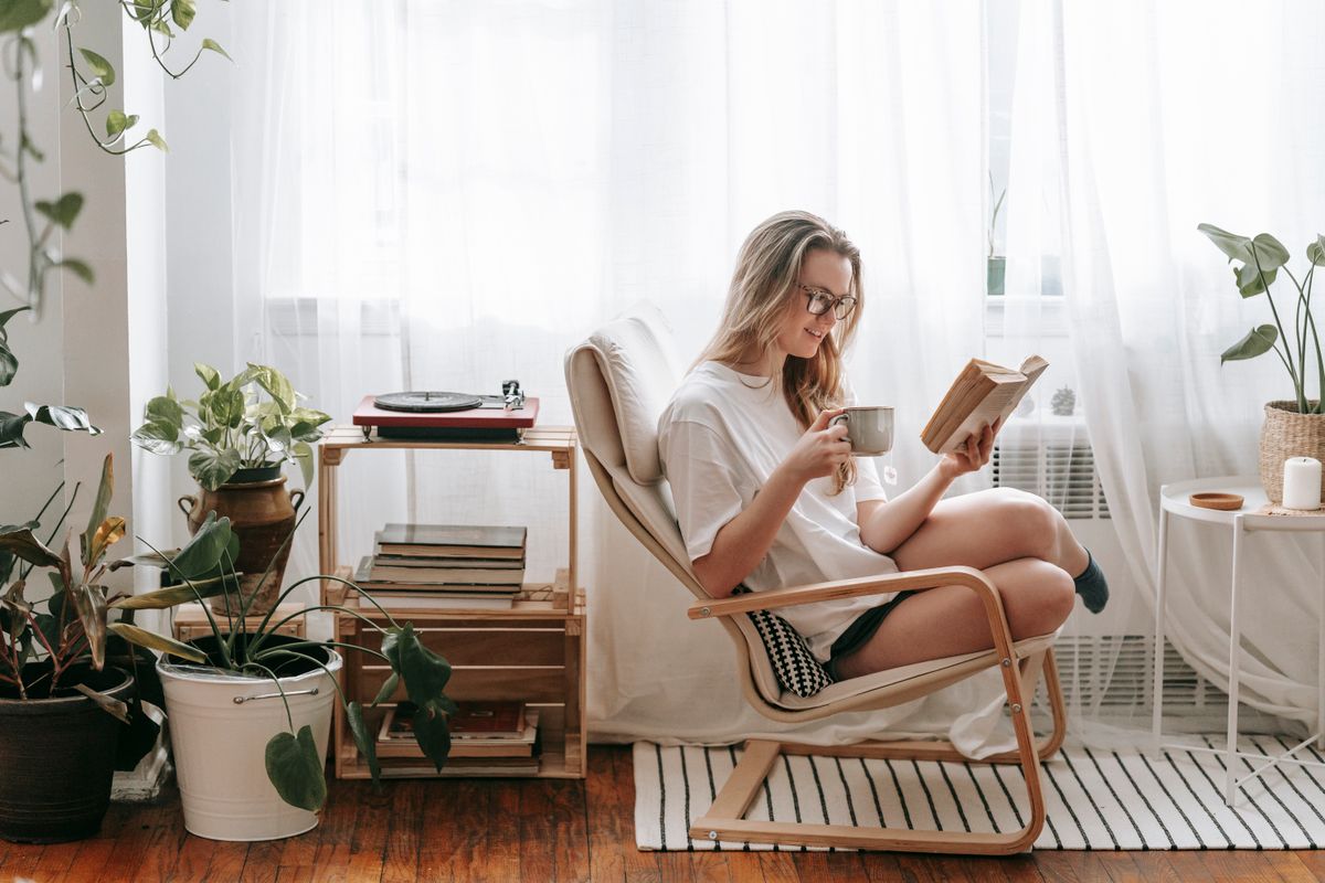 Woman reading a book in a cozy chair beside plants and books