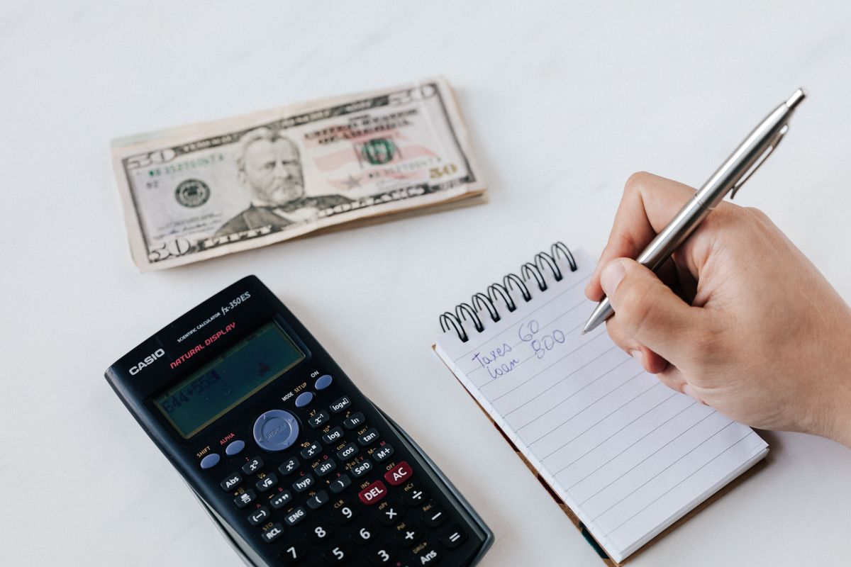 Hand writing a budget in a notebook beside a calculator and cash